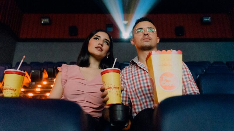 2 women sitting on blue leather chair holding white and red plastic cups proibição de entrar com alimentos no cinema