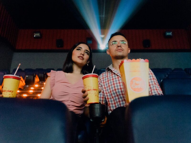 2 women sitting on blue leather chair holding white and red plastic cups proibição de entrar com alimentos no cinema